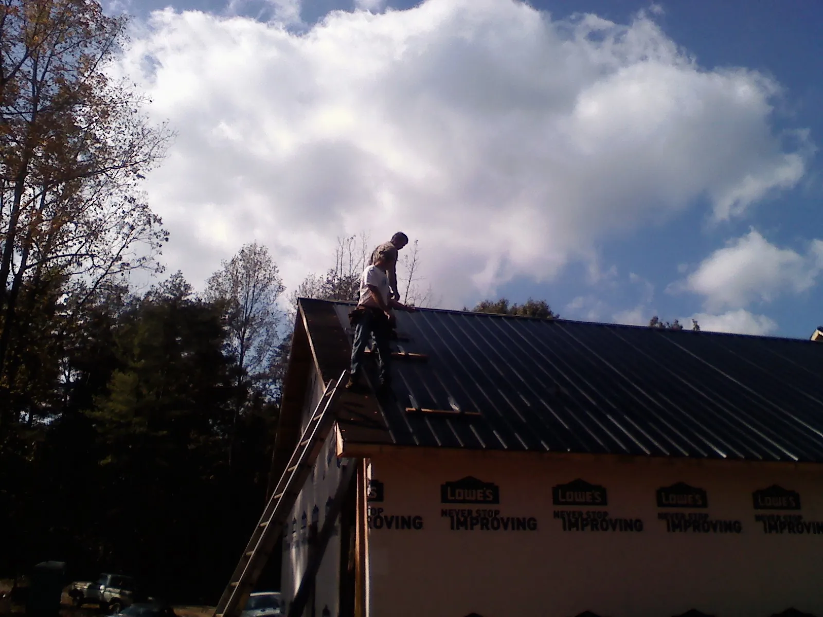 Roofer fastening dark metal panels high against a cloudy sky, from a Roof Inspection job in Gaston