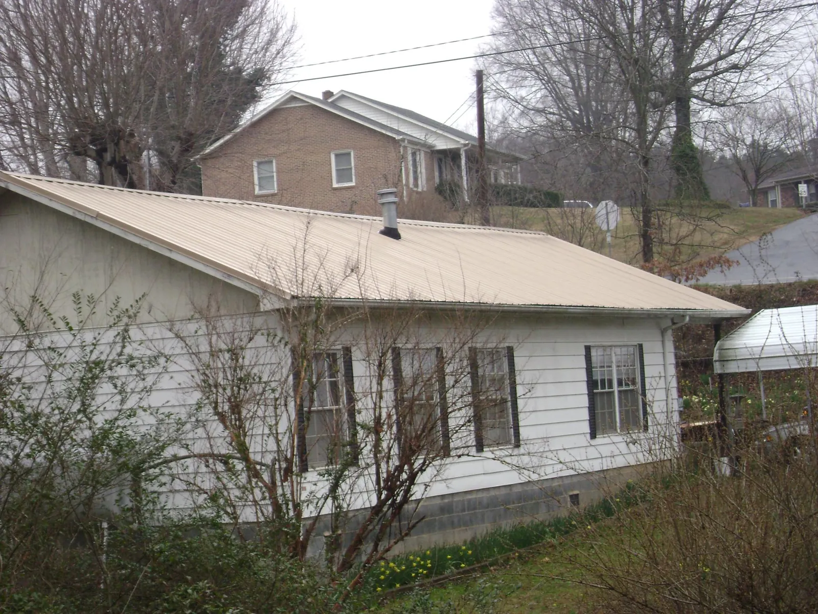 Tan metal roof on a white sided house set into a hillside — Commercial Roofing by Roofing Brothers in Gaston